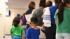 FILE - Photo provided by U.S. Immigration and Customs Enforcement shows mothers and their children standing in line at South Texas Family Residential Center in Dilley, Texas, Aug. 9, 2018.